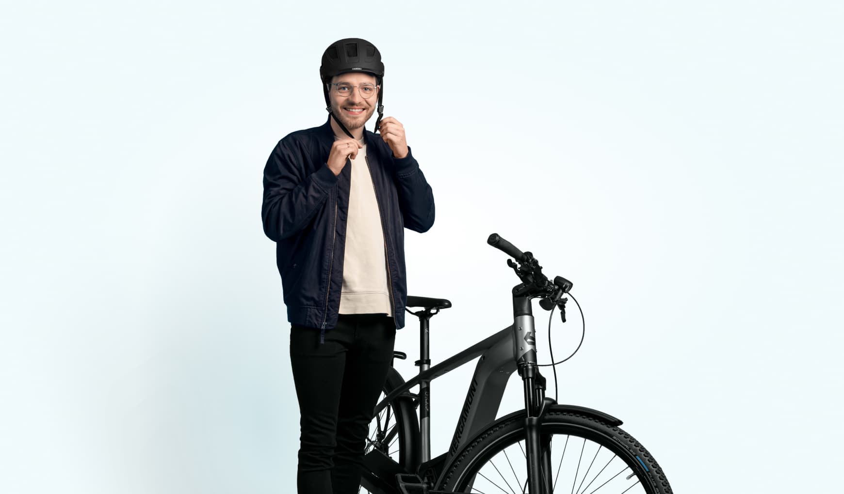 Eine Mann schliesst die Schnalle seines Fahrradhelms und steht lächelnd neben einem E-Bike.
