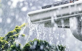 Ein Sturm mit Starkregen, der eine Dachrinne eines Hauses überlaufen lässt.