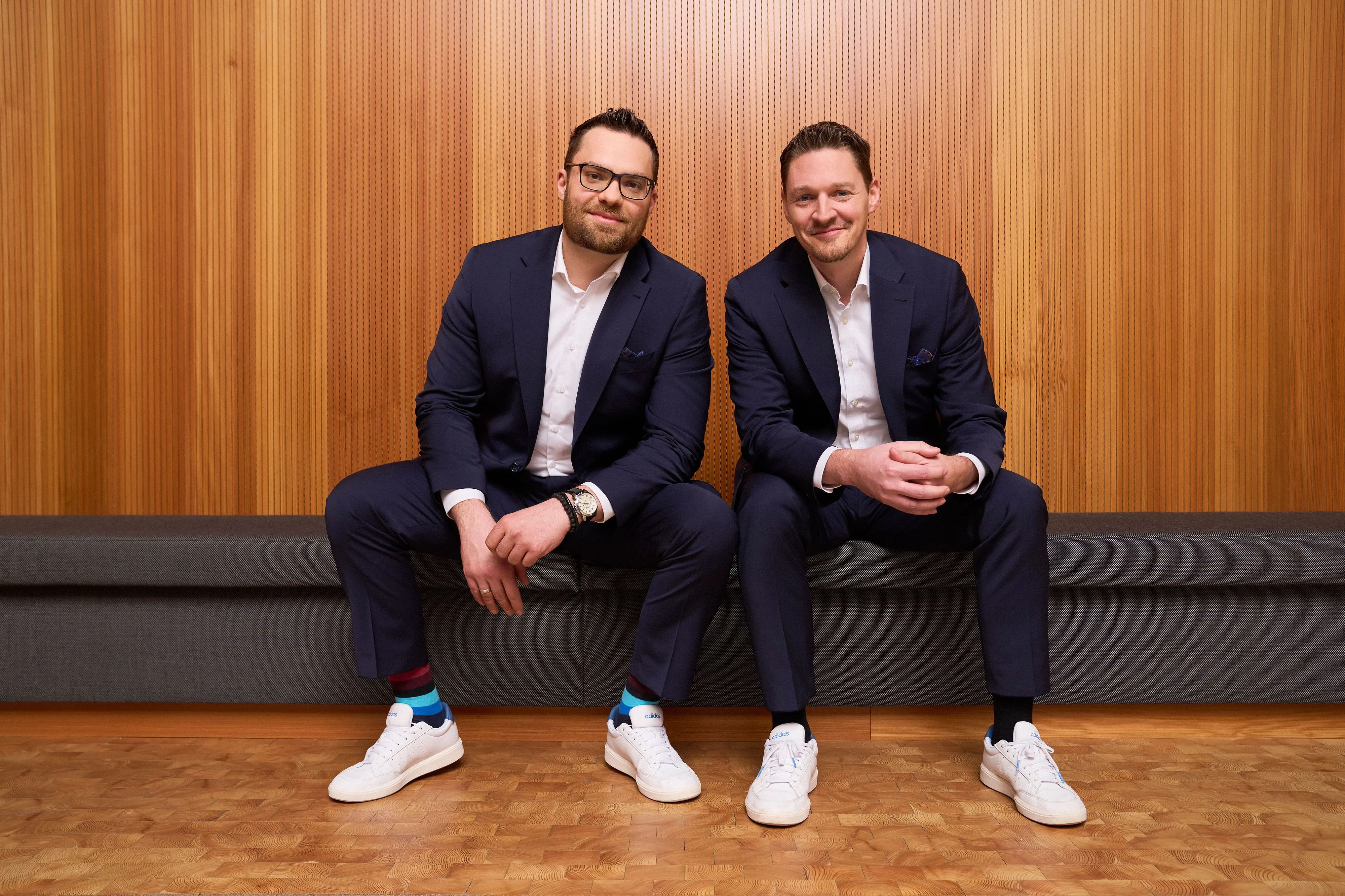 Julian Grauer (l) und Sven Tippelt (r) sitzen auf einer Bank im Campus der W&W-Gruppe.