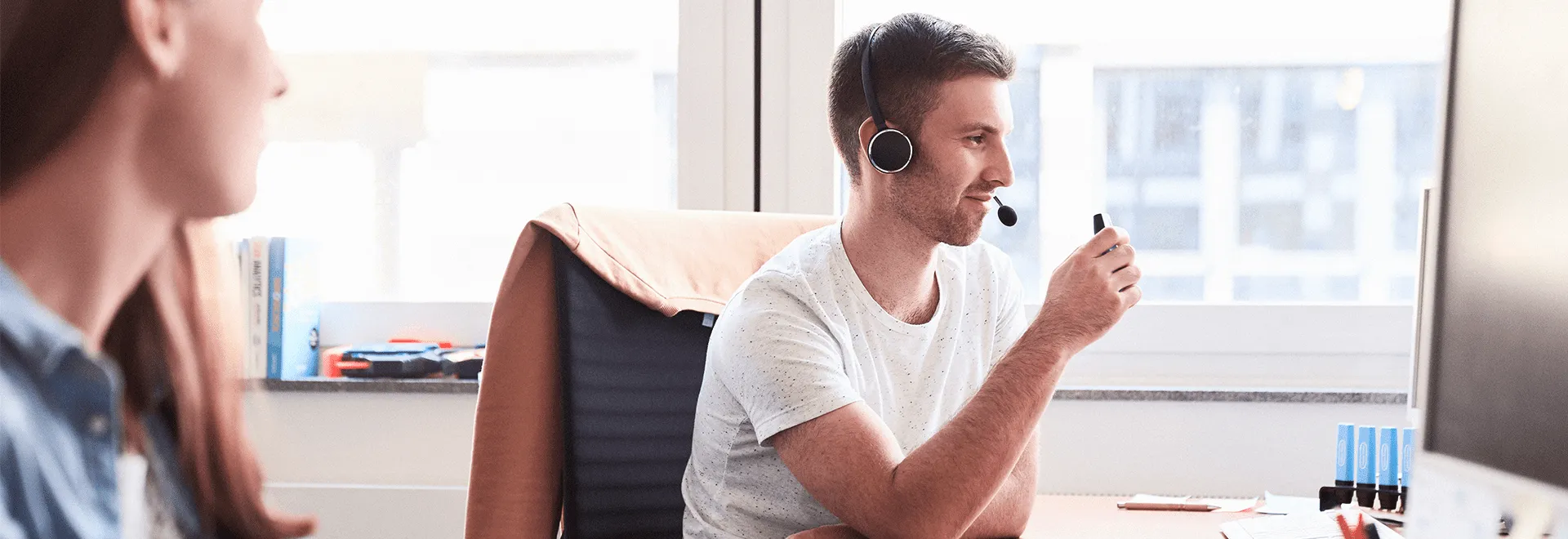 Volle Konzentration: Tobi am Schreibtisch mit Headset auf. Am Bildrand sieht man eine Kollegin sitzen.