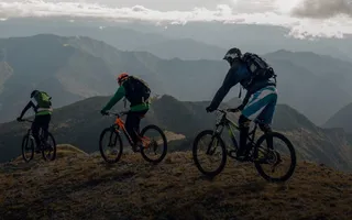 Drei Personen fahren Mountainbike im Gebirge. Für viele Sportarten eignet sich die Adam Riese Unfallversicherung.